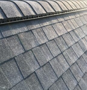 Close-up view of Expert Roof Ventilation by 256-ROOFERS. A roof showcasing durable asphalt shingles neatly aligned with ridge caps and a ridge vent for optimal attic ventilation and weather protection. 